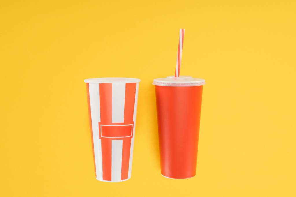 полосатое ведро попкорна и красная одноразовая чашка с соломой, изолированной на желтом
 - Фото, изображение