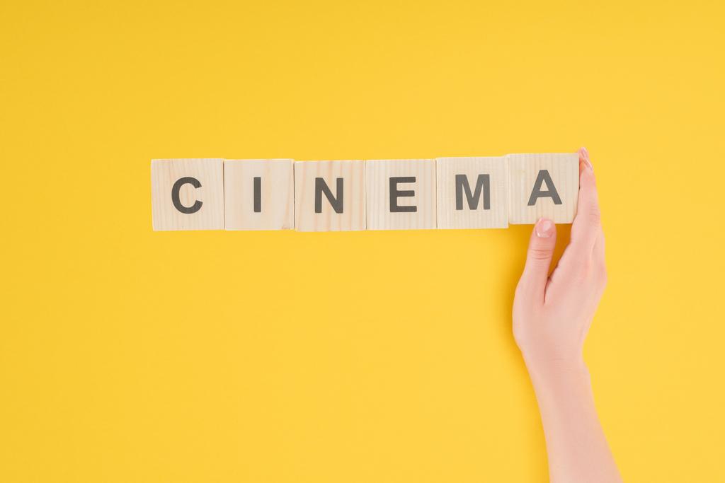 top view of female hand touching wooden cubes with "cinema" lettering isolated on yellow - Photo, Image