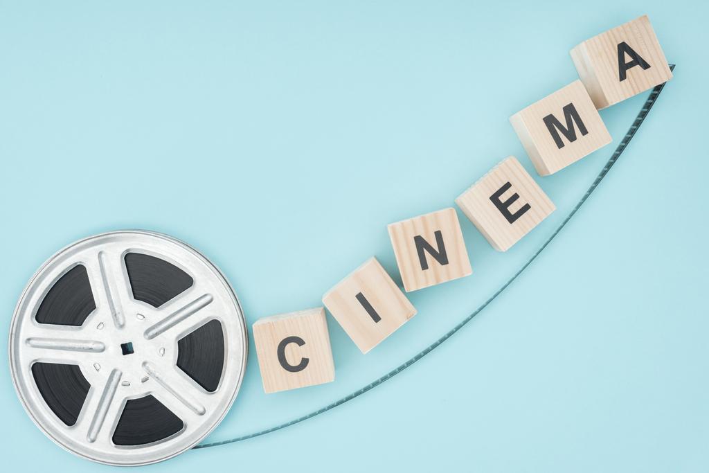 ξύλινα κύβοι με γράμματα «κινηματογράφος» και ρολό ταινία που απομονώνονται σε μπλε - Φωτογραφία, εικόνα