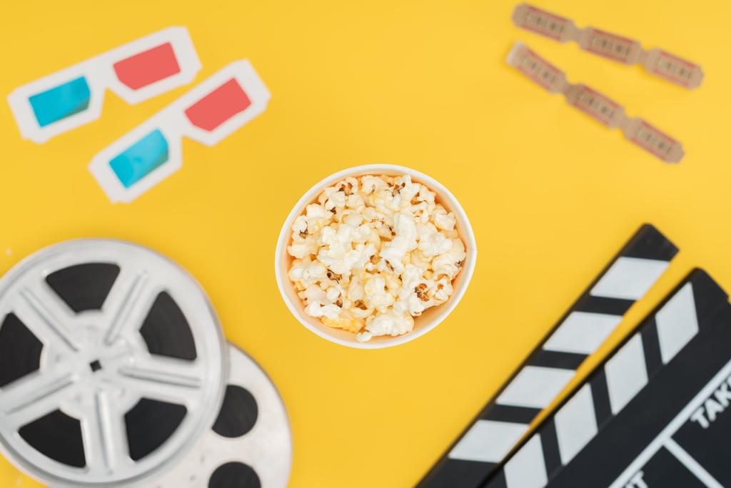 vista superior de clapperboard, carretes de película, gafas 3d, entradas de cine y palomitas de maíz cubo aislado en amarillo
 - Foto, imagen