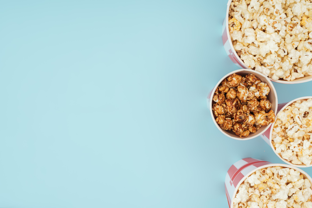 Ansicht von Eimern mit Popcorn in senkrechter Reihe isoliert auf blau - Foto, Bild