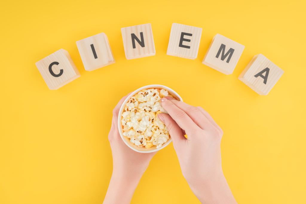 "sinema" yazı ve kova ve sarı izole alarak patlamış mısır holding eller ile tahta küpler üstten görünüm - Fotoğraf, Görsel