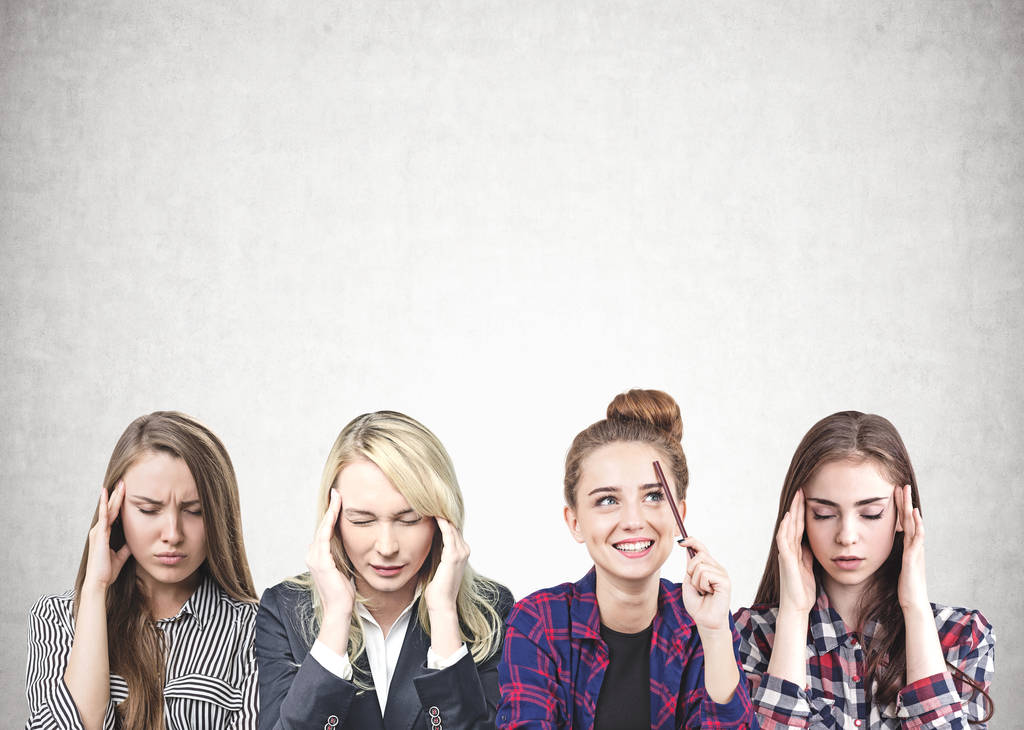 Ritratto di quattro belle giovani donne in abiti casual e formali sedute di fila vicino a un muro di cemento e che pensano intensamente. Scherzi?
 - Foto, immagini