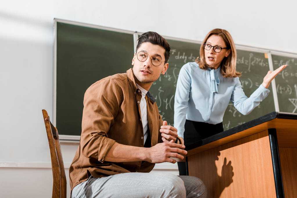 Enseignante insatisfaite debout près du tableau et parlant avec un élève en classe
  - Photo, image