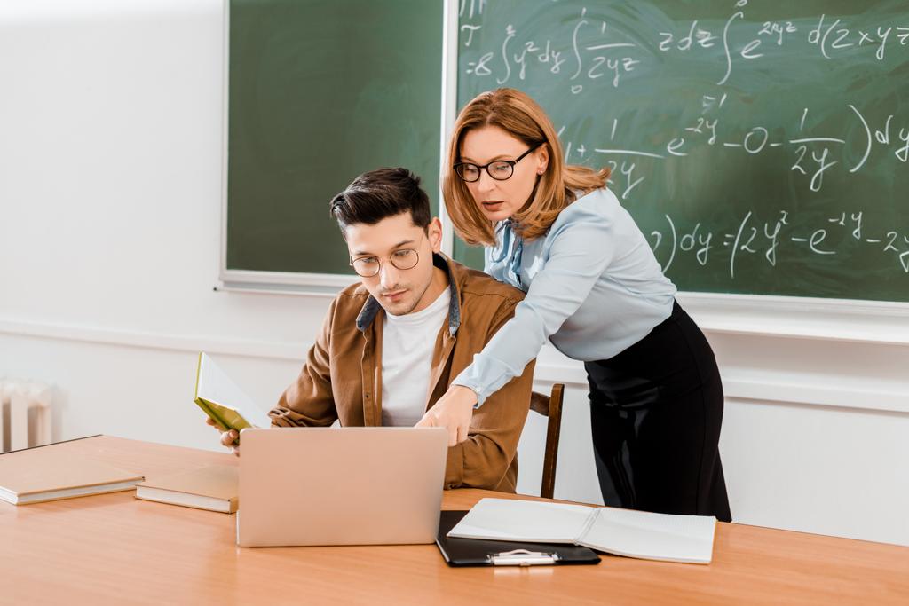 Lehrerin zeigt in der Klasse auf Laptop neben Schülerin - Foto, Bild