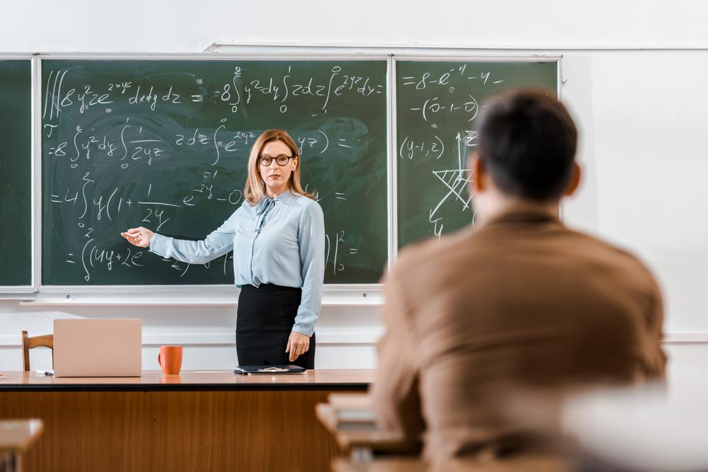 Lehrer zeigt mit Schüler auf Gleichungen im Klassenzimmer  - Foto, Bild
