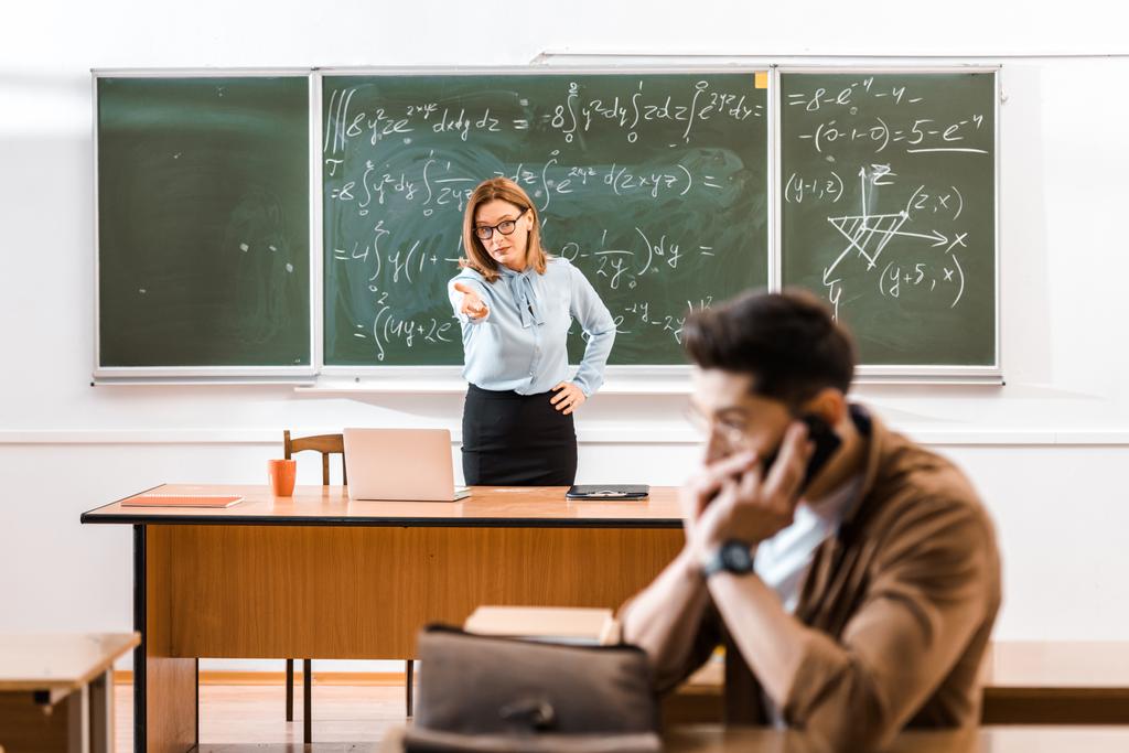 Teacher standing near chalkboard and speaking with student who talking on smartphone  - Photo, Image
