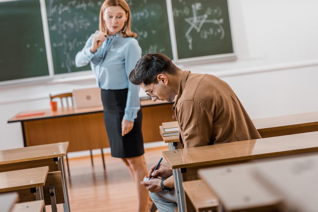 accent sélectif de l'enseignante insatisfaite regardant l'étudiant mâle tricher pendant l'examen en classe
 - Photo, image