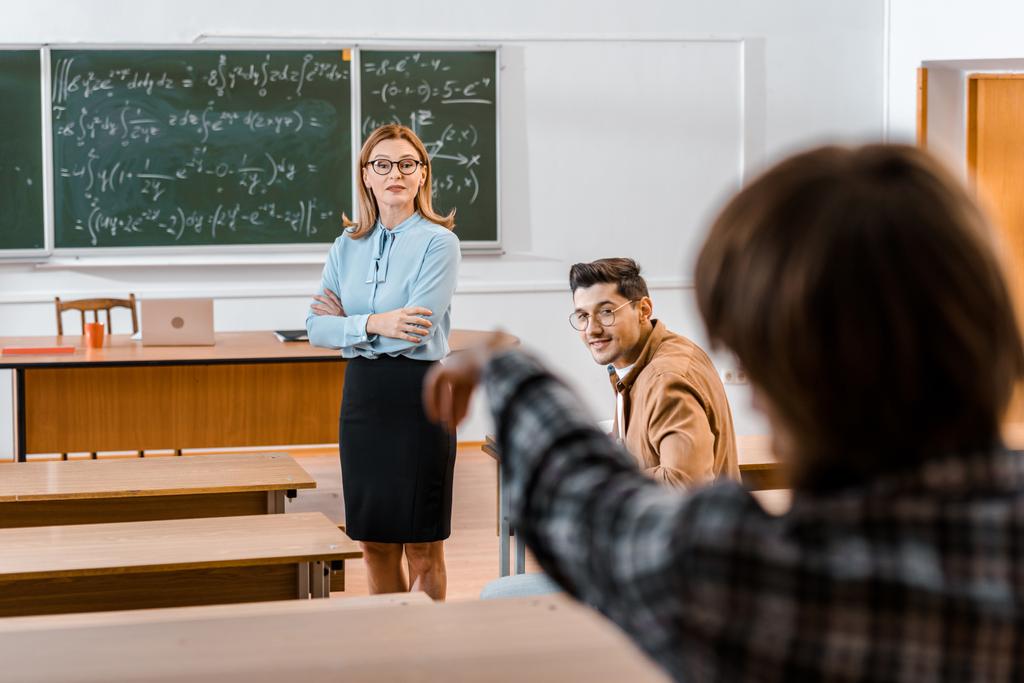 selectieve aandacht van vrouwelijke leraar les materiaal terwijl mannelijke student klasgenoot kijken uit te leggen - Foto, afbeelding