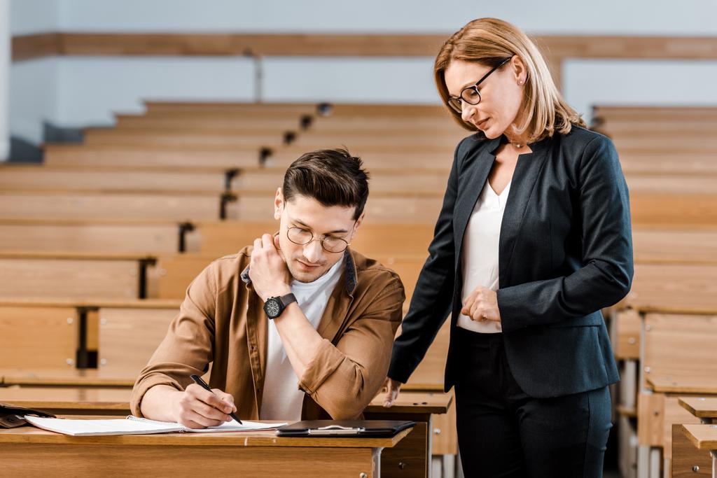 žena vysokoškolský učitel při pohledu na muže student psaní zkoušky v učebně - Fotografie, Obrázek