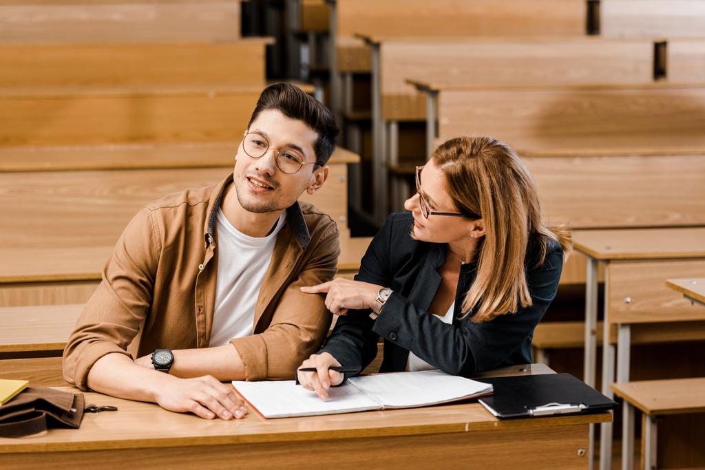 profesora universitaria sentada en el escritorio con un estudiante masculino durante el examen en el aula
 - Foto, Imagen