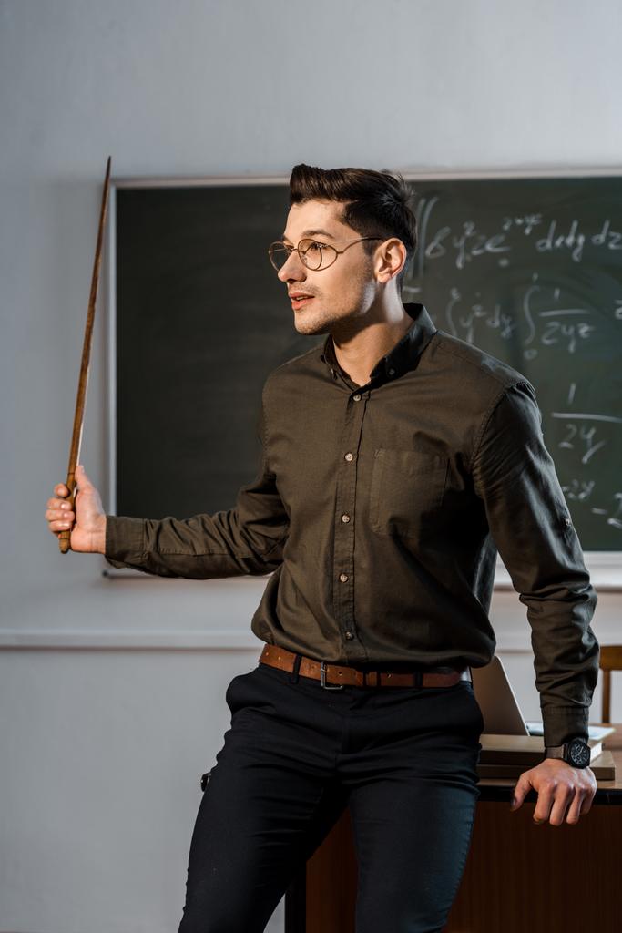 mężczyzna nauczyciel w wizytowym i okulary przytrzymując wskaźnik drewniane i wyjaśniając równania w klasie - Zdjęcie, obraz