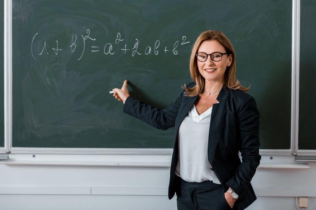 professora apontando com o dedo para a equação matemática em quadro-negro na aula
 - Foto, Imagem