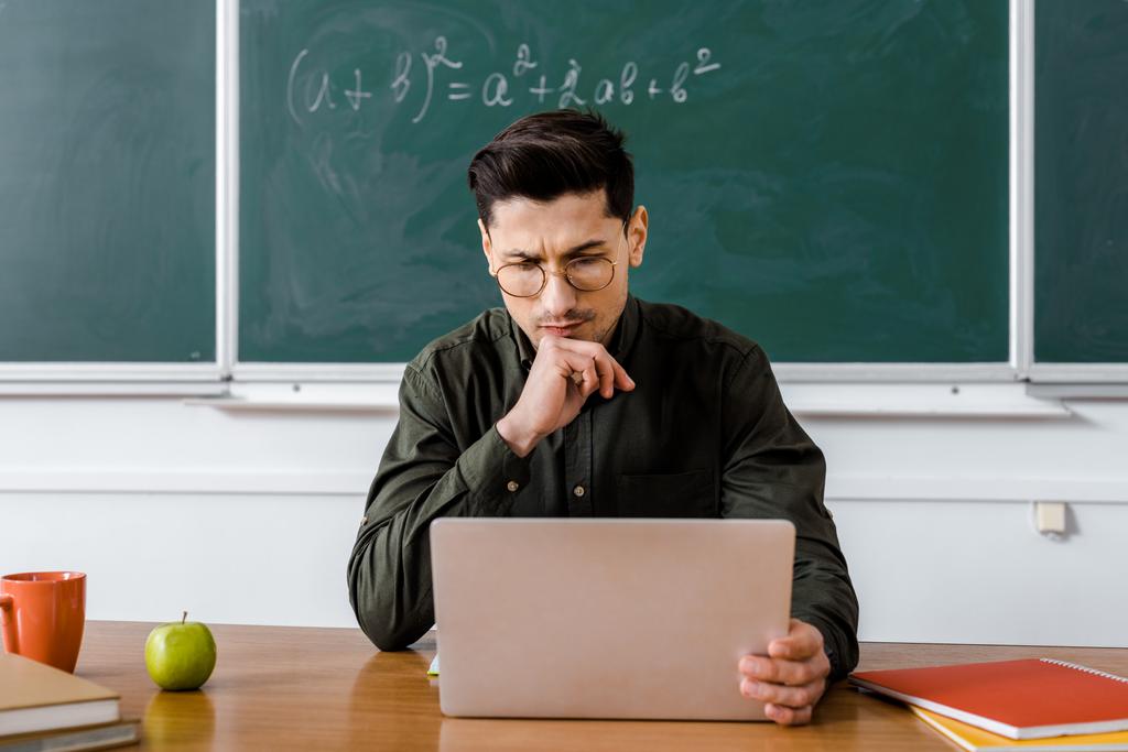 cher professeur masculin dans des lunettes assis au bureau et en utilisant l'ordinateur dans la classe
 - Photo, image