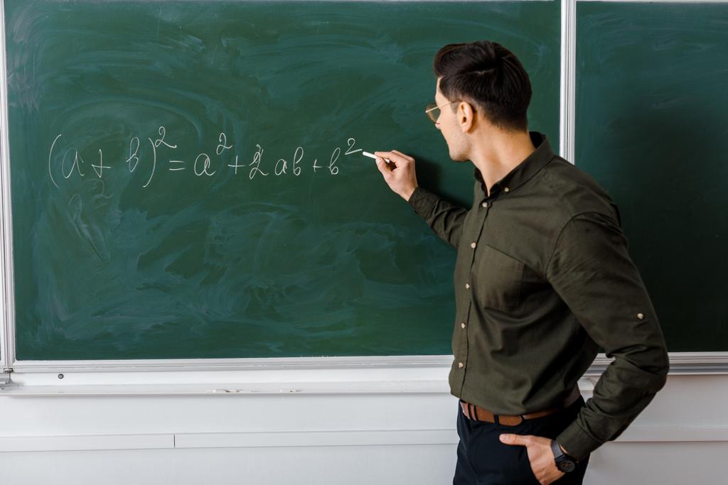 数学のクラスの黒板に方程式を書く正式な摩耗で男性教師 ロイヤリティフリー写真 画像素材