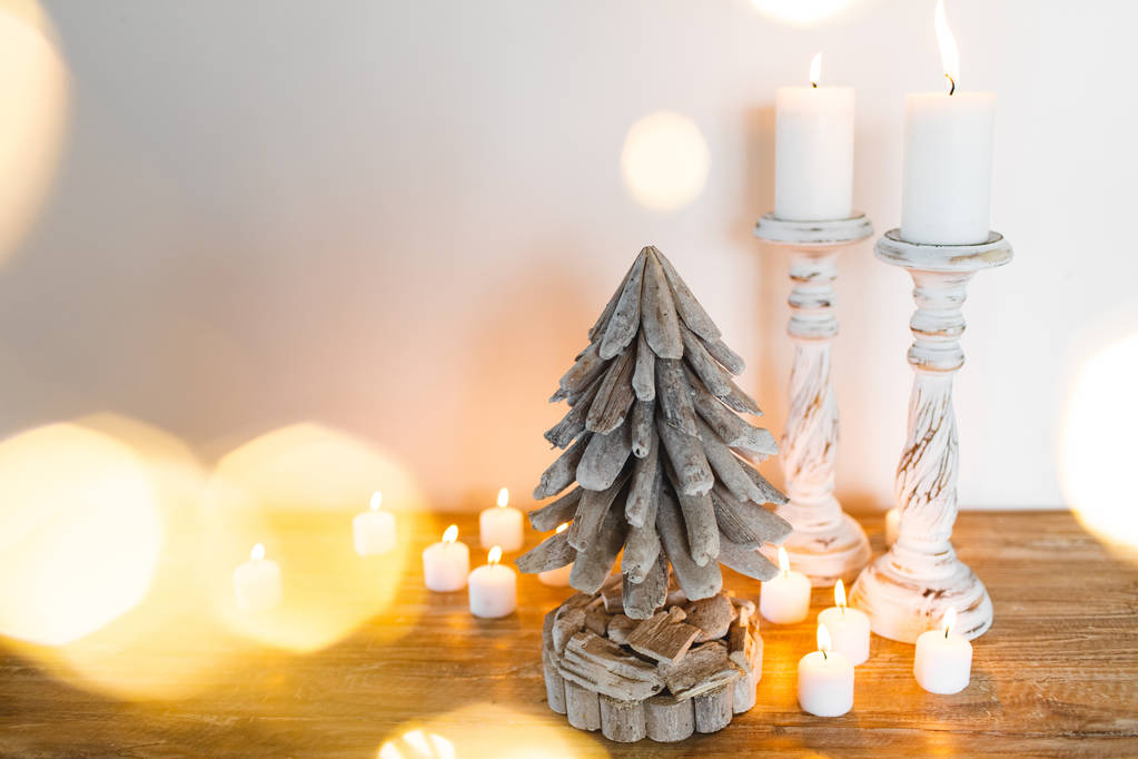 Белая деревянная украшенная елка со свечами и золотыми размытыми сияющими огнями вокруг. Место для смс. Праздничная концепция ручной работы
 - Фото, изображение