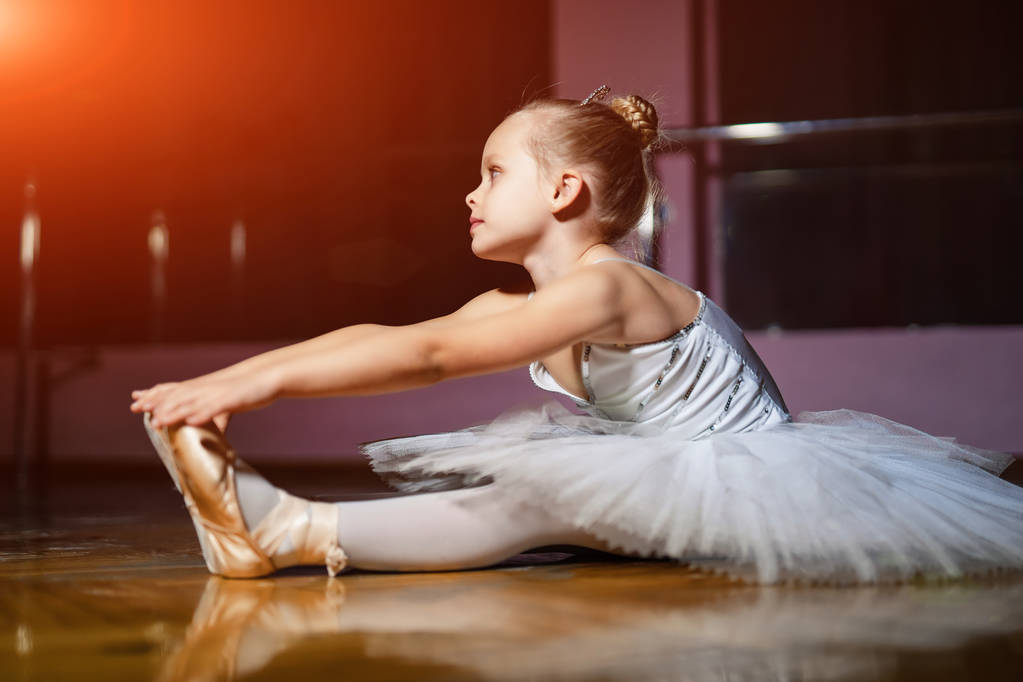 Küçük sevimli genç balerin odunsu zemin ve dans stüdyosu zemin üzerine oturan beyaz elbiseli. Profesyonel balerin, klasik dans okulu olmak rüya güzel kız bebek - Fotoğraf, Görsel