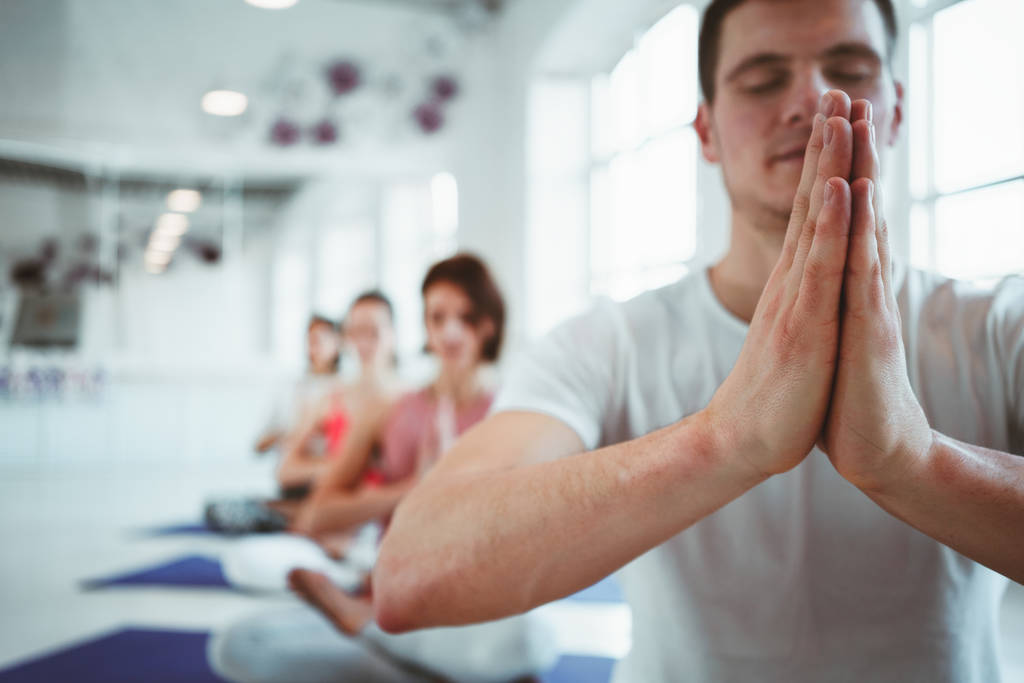 El entrenador masculino entrena a grupo de mujeres ejercicios de yoga para mantener la atención médica en clase blanca. La gente junta practica yoga posa
 - Foto, Imagen