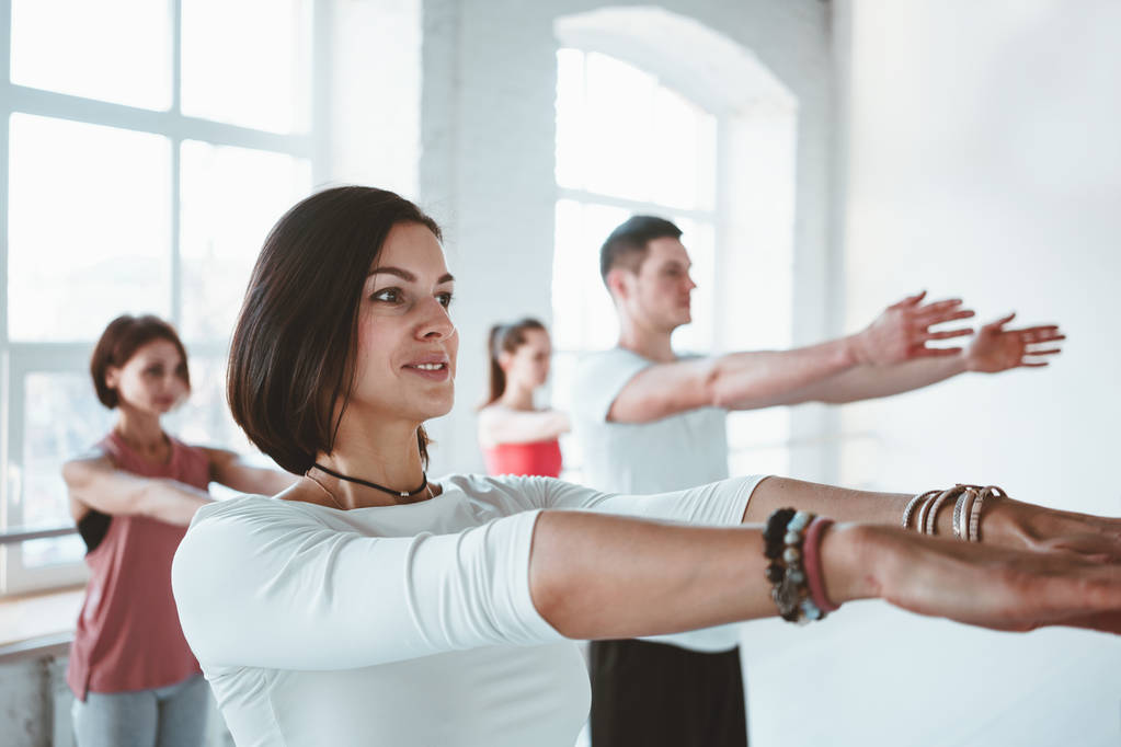 Portret van sterke fit vrouw opleiding yoga vormt op fitness mat samen met groep mensen op de achtergrond. Healthe zorg en lifestyl - Foto, afbeelding