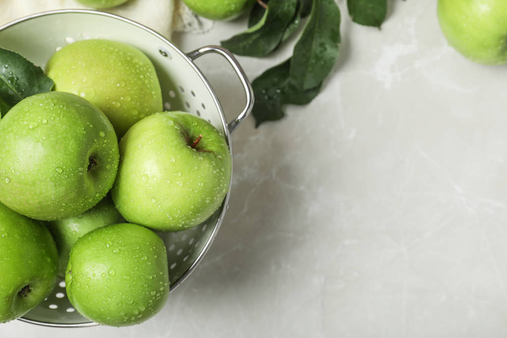 Сочные зеленые яблоки в дуршлаге и место для текста на столе
 - Фото, изображение