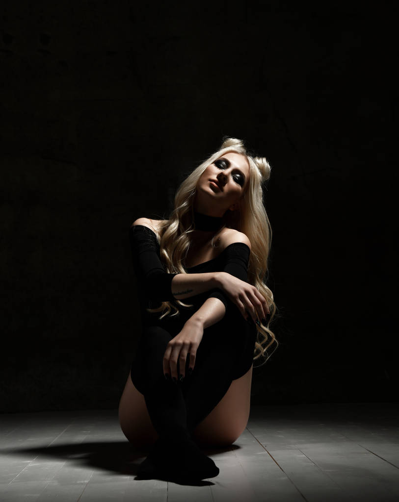 Молода сексуальна блондинка модна жінка сидить на підлозі в чорній сукні на темному нічному фоні
 - Фото, зображення
