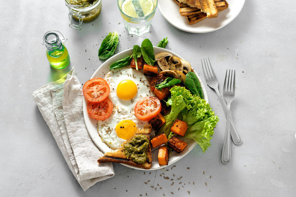 Piatto colazione con uova fritte, verdure, funghi e pane tostato su sfondo grigio cemento
 - Foto, immagini