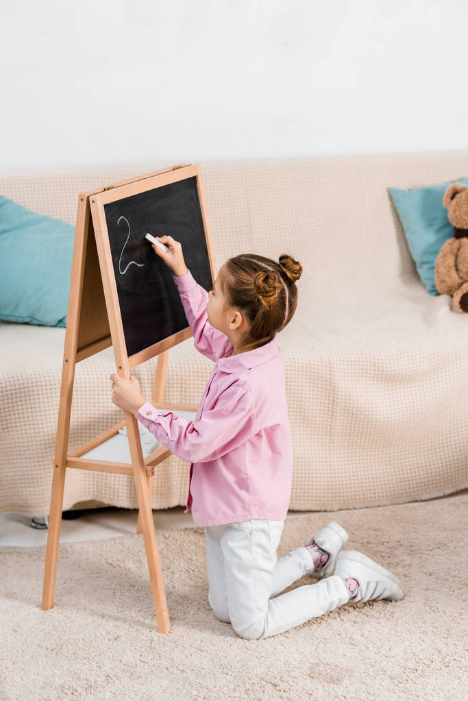 wysoki kąt widzenia słodkie dziecko klęczy na dywanie i pisanie na tablicy - Zdjęcie, obraz