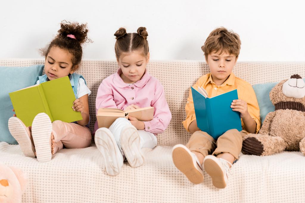 adorabili bambini multietnici seduti sul divano e leggere libri insieme
 - Foto, immagini