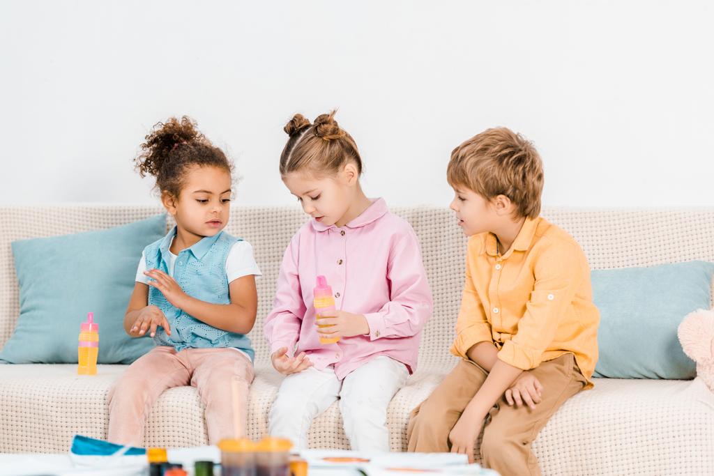 rozkošný mnohonárodnostní děti sedí na pohovce a hrát si s mýdlové bubliny     - Fotografie, Obrázek