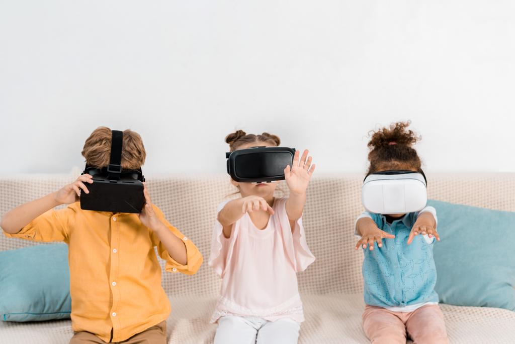 милые маленькие дети сидят на диване и используют гарнитуры виртуальной реальности
  - Фото, изображение