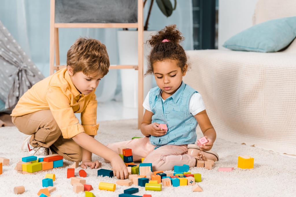 schattig multi-etnisch kinderen spelen met kleurrijke houten blokken op tapijt - Foto, afbeelding