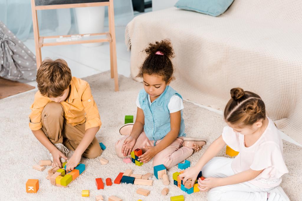 pohled z vysokého úhlu rozkošný mnohonárodnostní dětí hraje s barevné kostky na koberci   - Fotografie, Obrázek