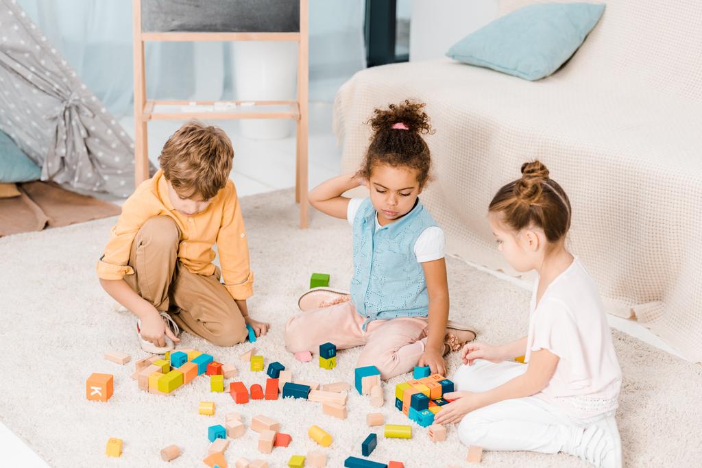 високий кут зору чарівних багатоетнічних дітей, які грають з барвистими кубиками на килимі
   - Фото, зображення