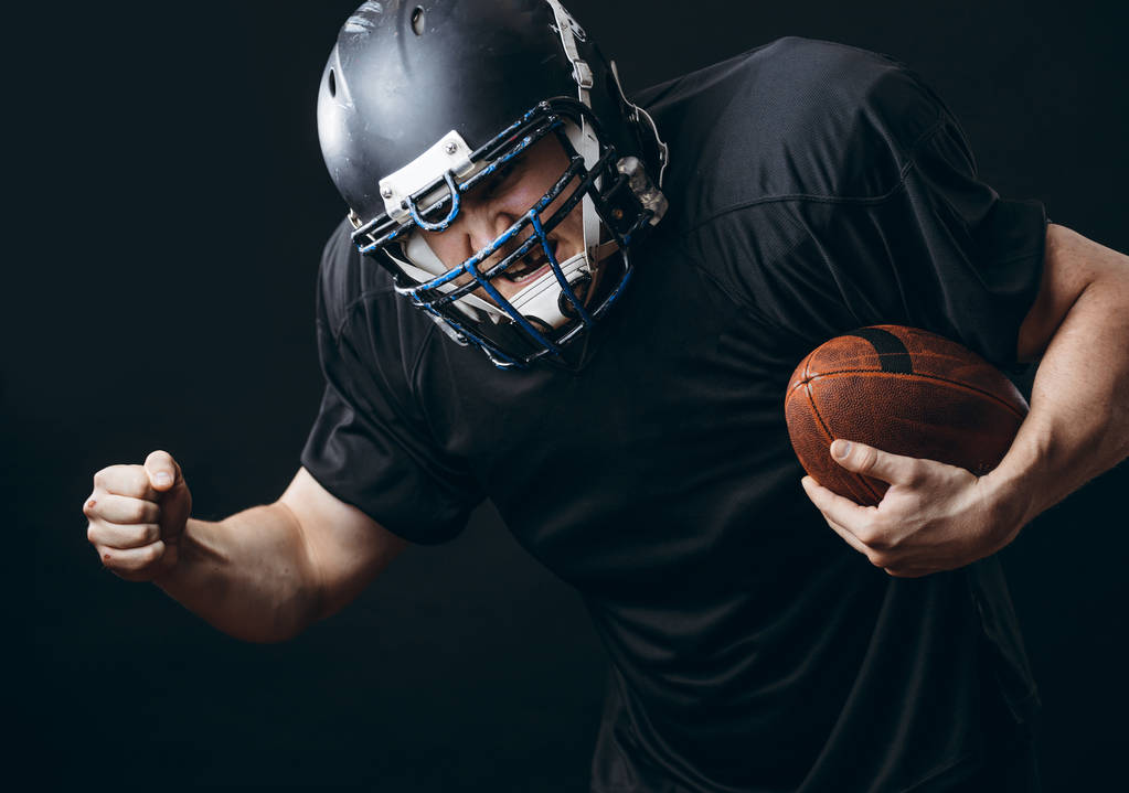 jugador de fútbol americano deportista en acción aislado sobre la pared de estudio negro - Foto, Imagen