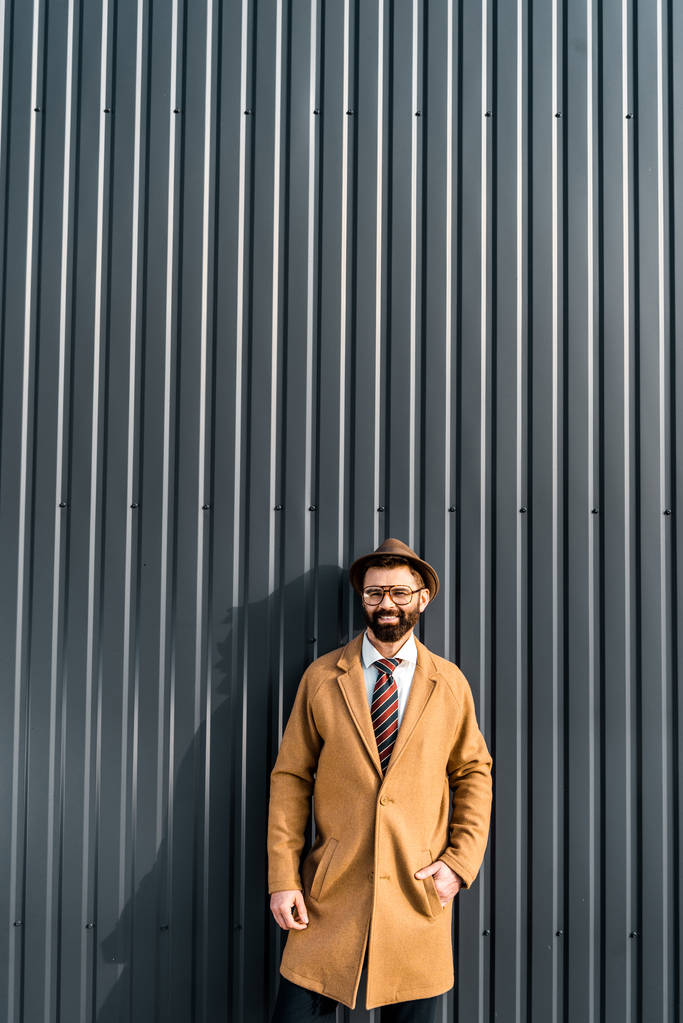homem de negócios sorridente no casaco de pé perto da parede texturizada
 - Foto, Imagem