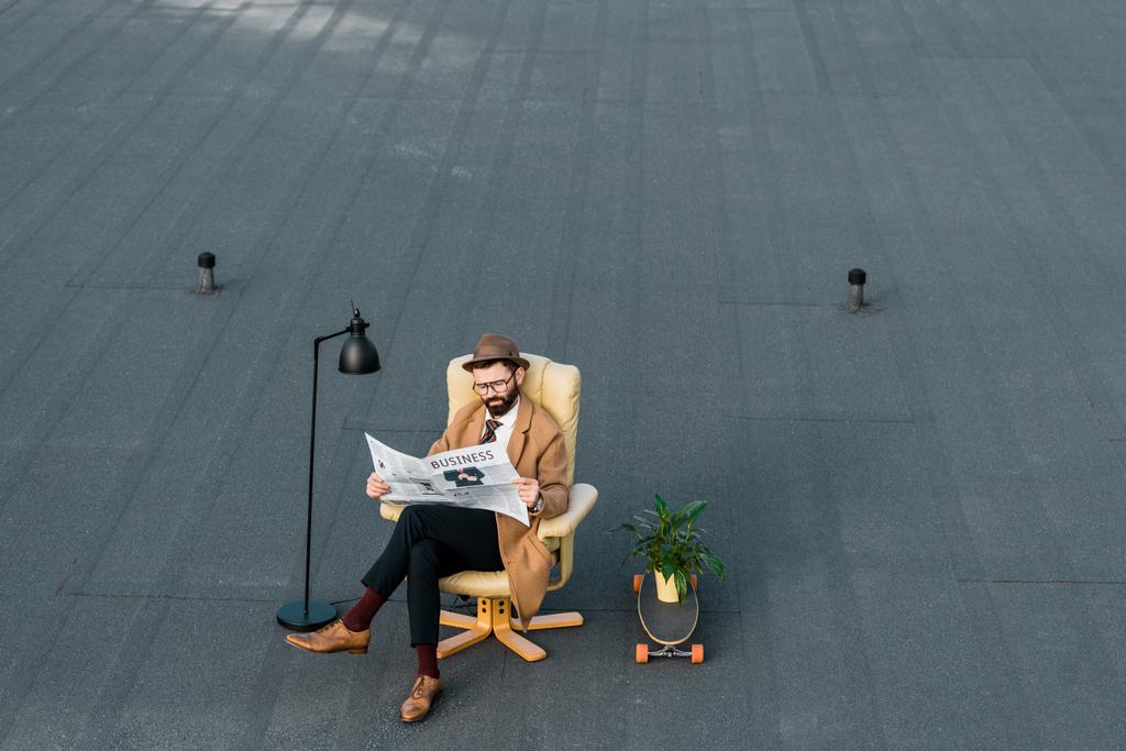 дорослий бородатий бізнесмен сидить у кріслі і читає газету на даху
  - Фото, зображення