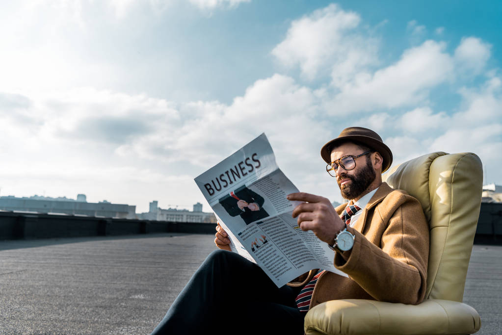 дорослий чоловік в окулярах і капелюсі читає бізнес-газета в кріслі на даху
 - Фото, зображення