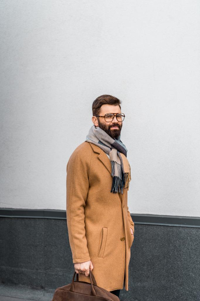 Бородатый бизнесмен, стоящий в бежевом пальто и держащий сумку
  - Фото, изображение