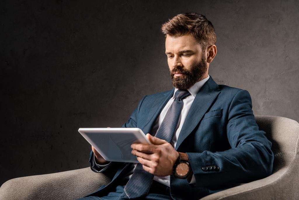 σοβαρός επιχειρηματίας χρησιμοποιώντας ψηφιακό tablet και κάθεται στην πολυθρόνα  - Φωτογραφία, εικόνα