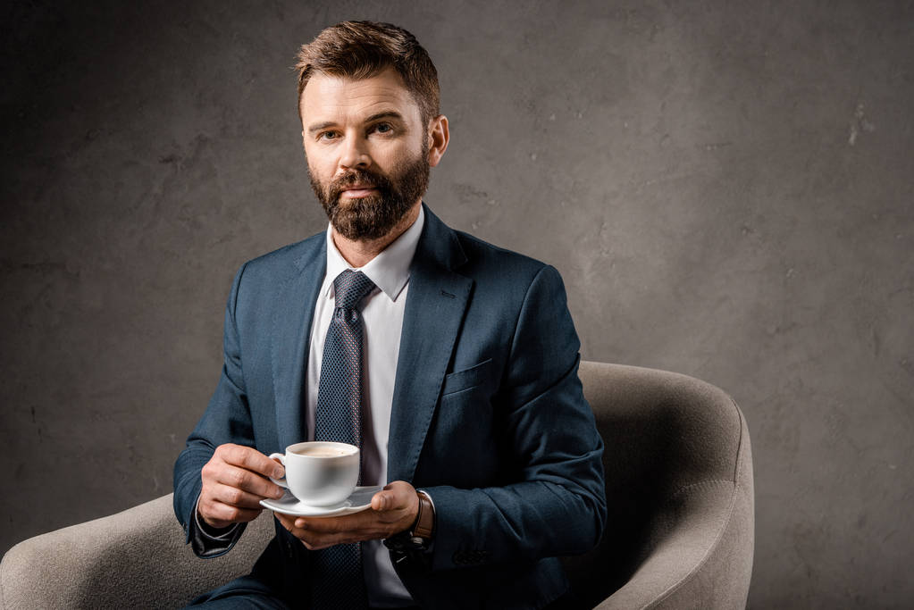homem de negócios sério sentado em poltrona com xícara de café
  - Foto, Imagem