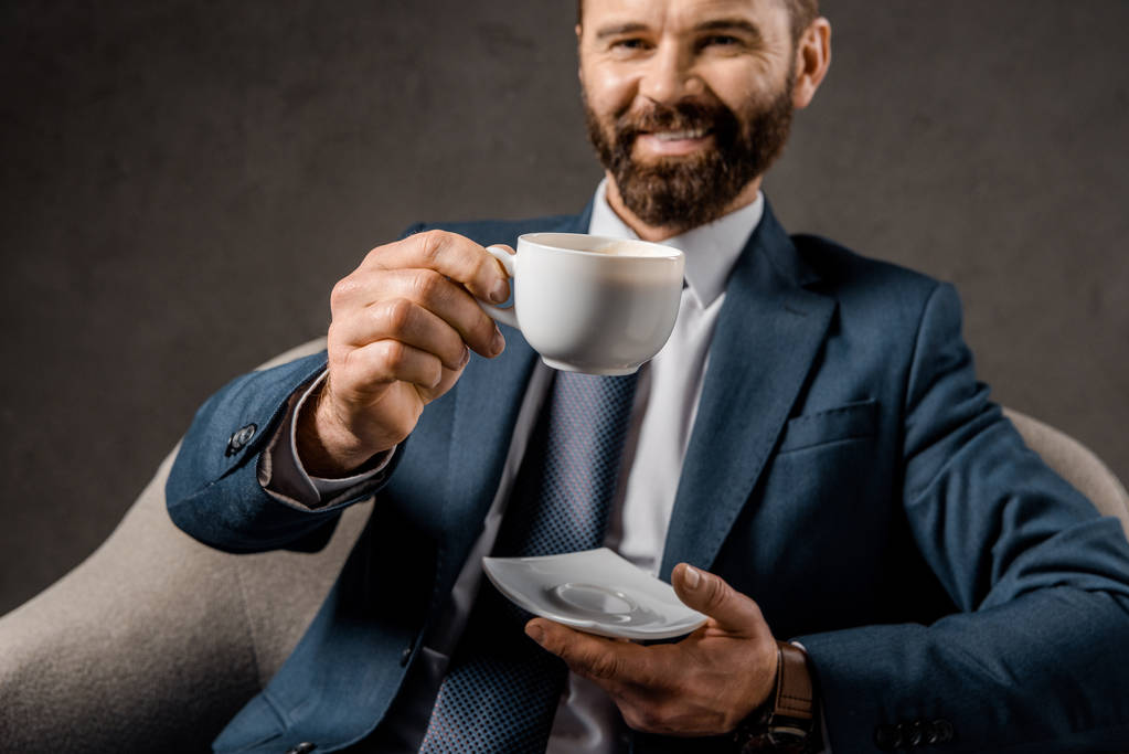 enfoque selectivo de la taza con café con hombre de negocios barbudo en el fondo
 - Foto, imagen