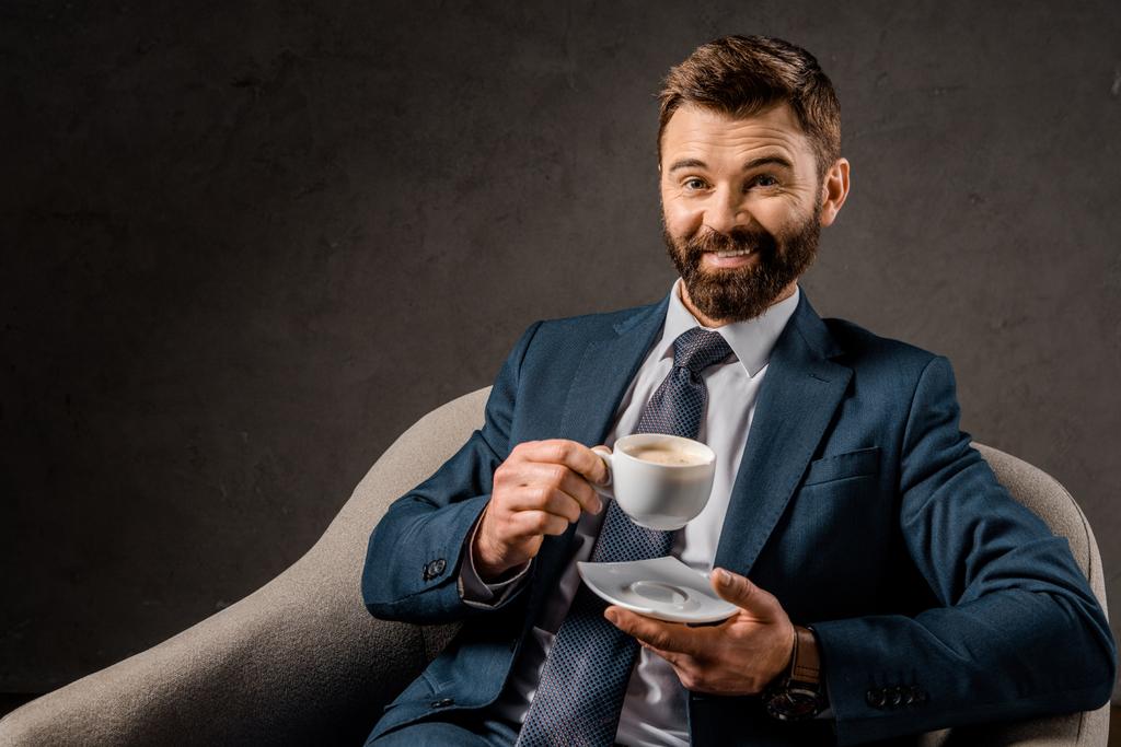homme d'affaires joyeux tenant tasse de café et assis dans le fauteuil
 - Photo, image
