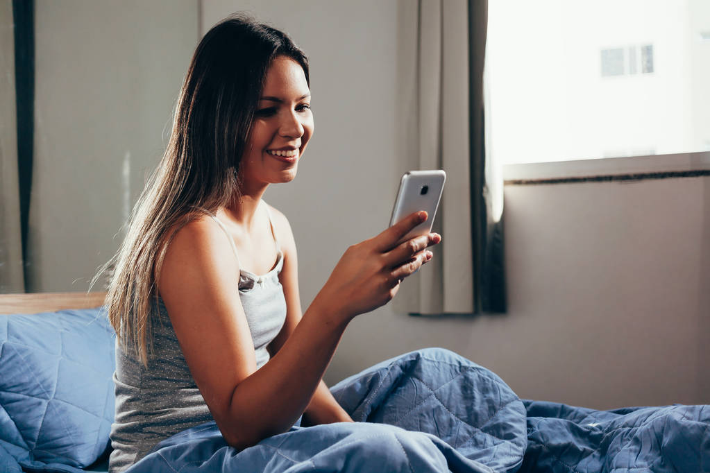 Mulher relaxada em casa lendo uma mensagem de texto em seu quarto
 - Foto, Imagem