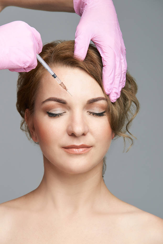 Inyección de aguja facial. El procedimiento de cosmetología de una joven. Guantes médicos. - Foto, imagen