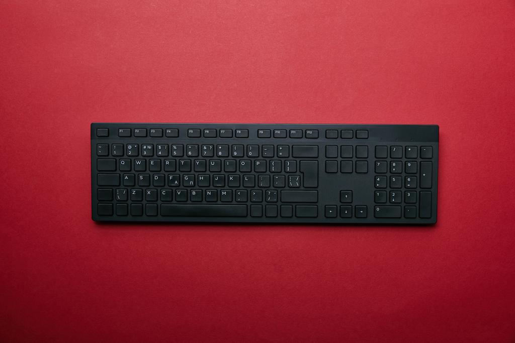 Pohled shora na černé počítačová klávesnice na červeném pozadí  - Fotografie, Obrázek
