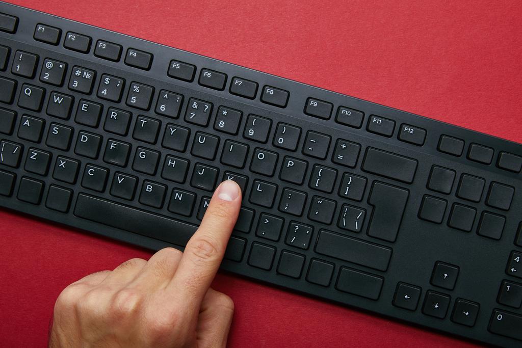 Oříznutý pohled člověka stlačením tlačítka na černé počítačovou klávesnici na červeném pozadí  - Fotografie, Obrázek