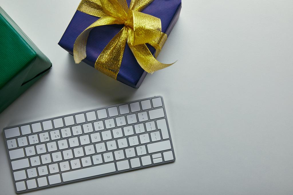 Vue recadrée des cadeaux près du clavier d'ordinateur blanc sur fond gris
  - Photo, image