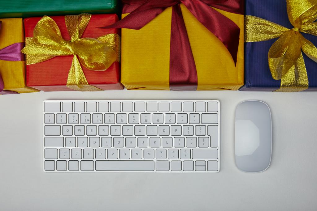 Вид зверху на подарунки поблизу комп'ютерної клавіатури та комп'ютерної миші на білому тлі
  - Фото, зображення