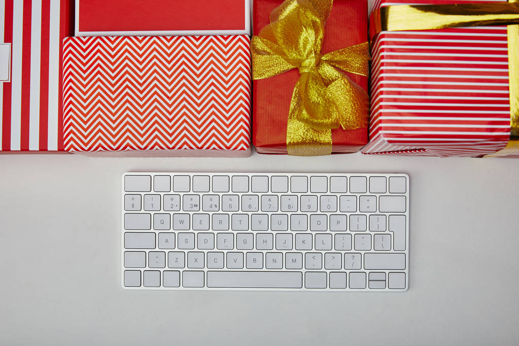 Vue du dessus des cadeaux colorés près du clavier d'ordinateur blanc sur fond blanc
  - Photo, image