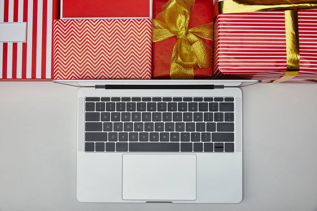 Вид зверху на ноутбук біля загорнутих барвистих подарунків
  - Фото, зображення